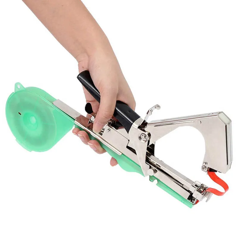 Рука держит тапенер для подвязки растений