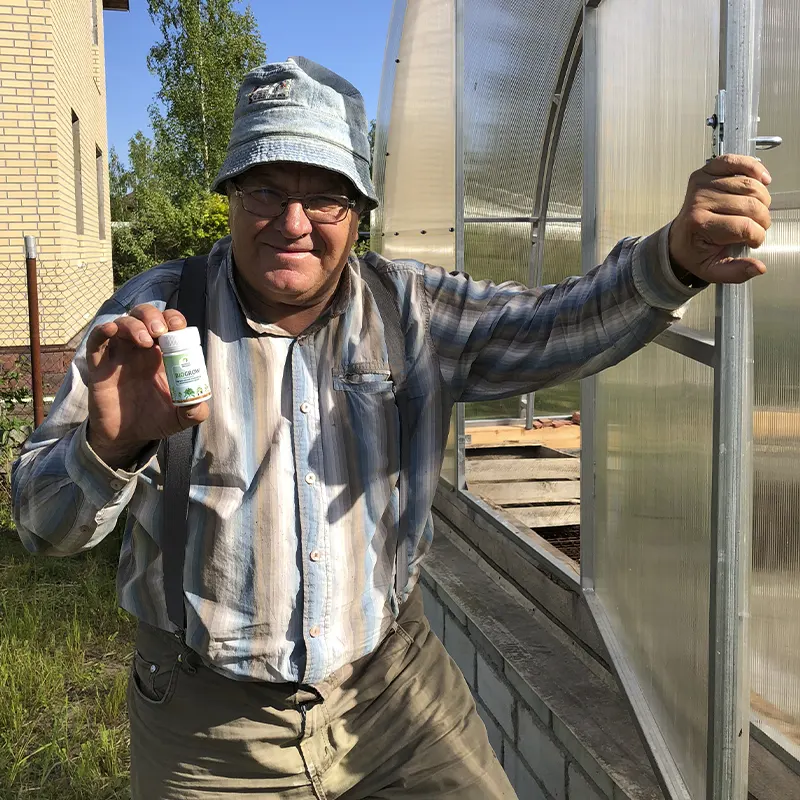 Садовод мужчина стоя рядом с теплицей показывается удобрение BioGrow