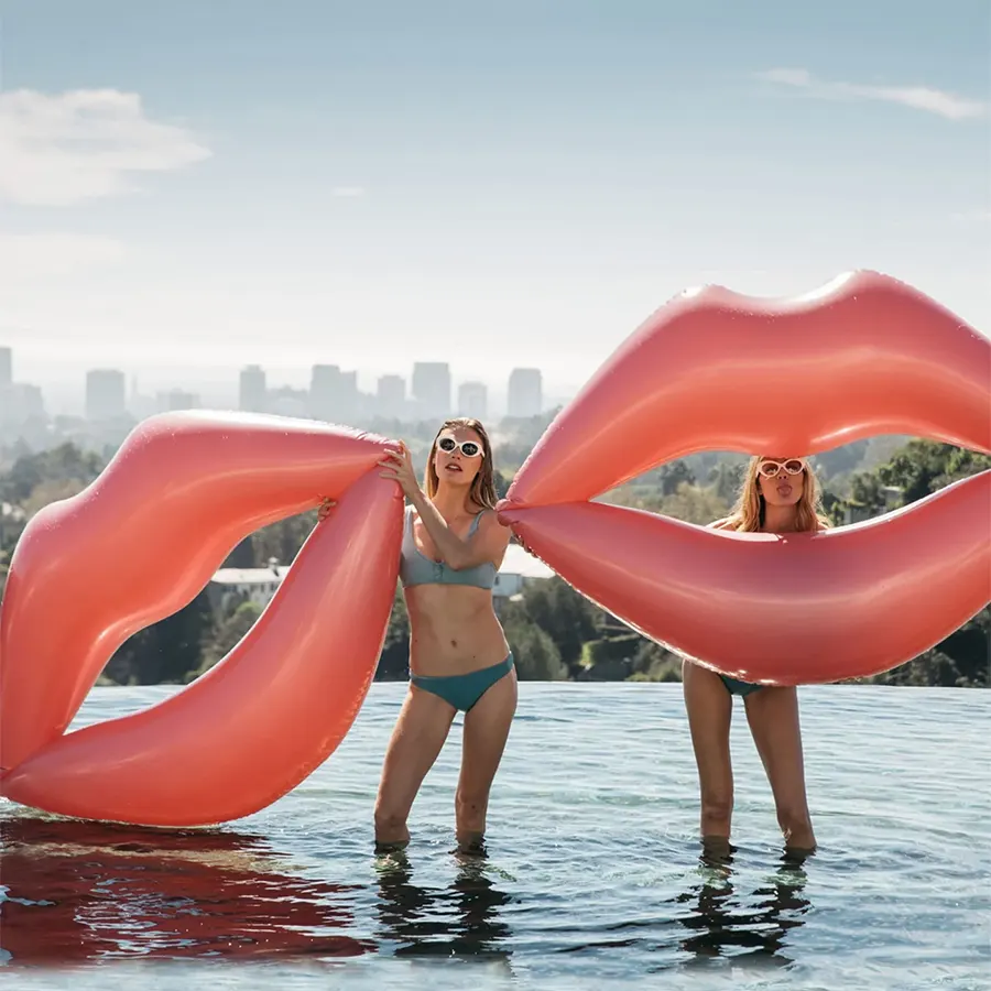 Две девушка держат надувные круги в виде розовых губ стоя в воде