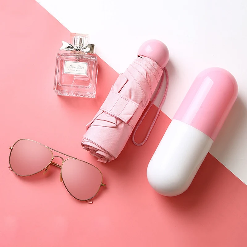 Очки, парфюм, зонт и капсуле лежат на бело-розовом фоне