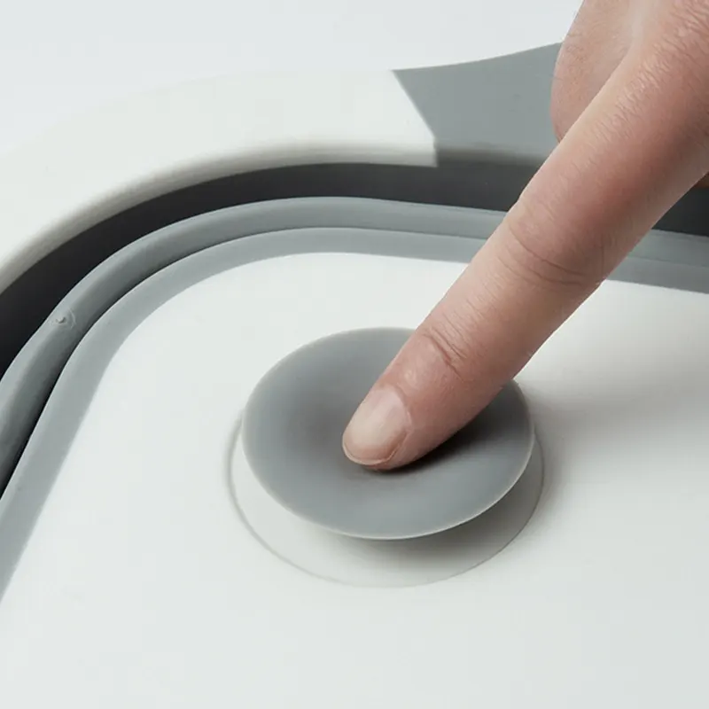 Палец нажимает на клапан для слива воды из складной разделочной доски дуршлага