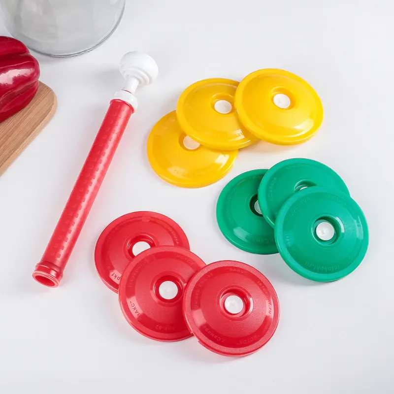 Вакуумные крышки трёх цветов и красный насос лежат на столе